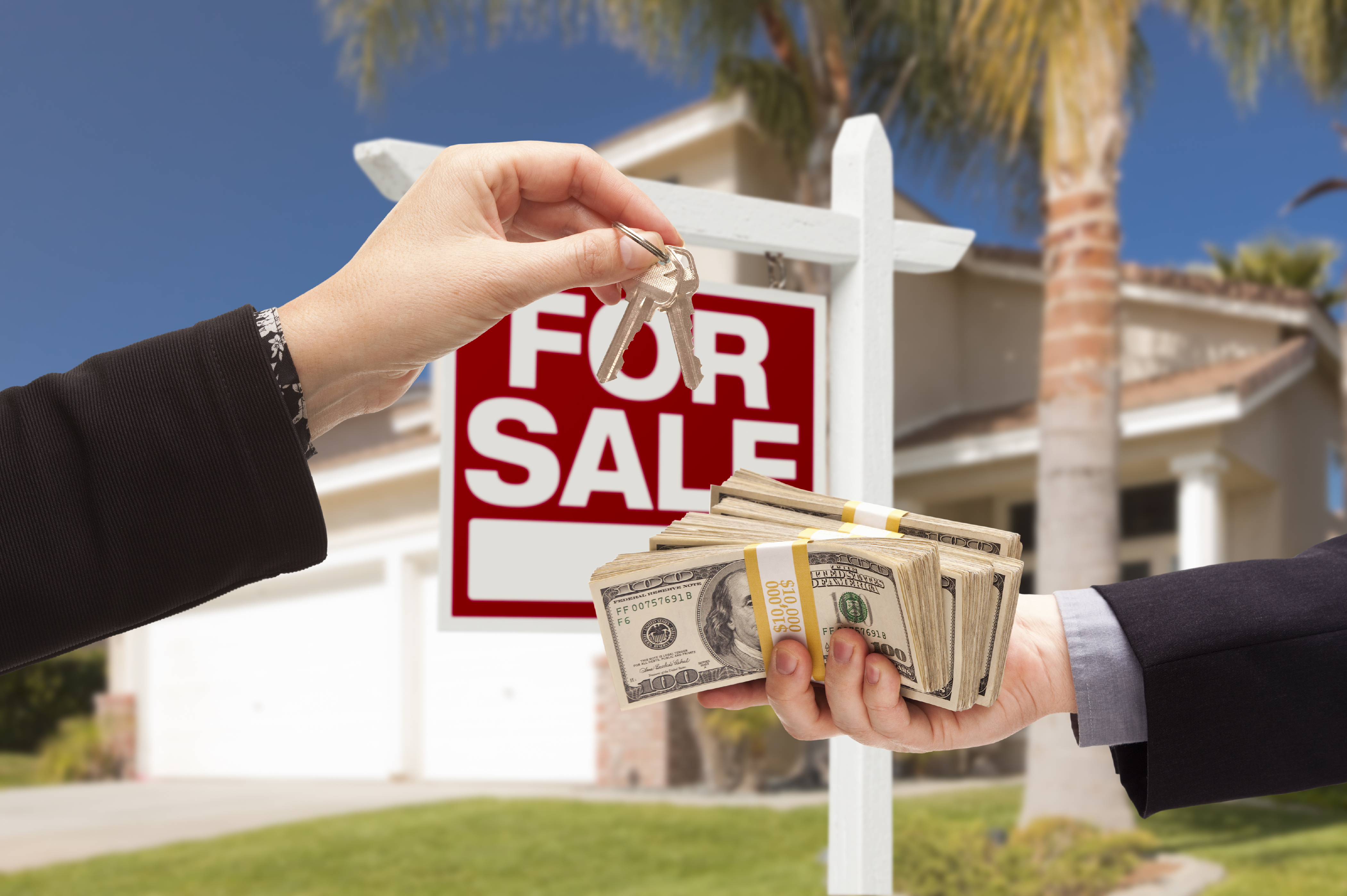 Agent Handing Over Keys as Buyer is Handing Over Cash for House with Home and For Sale Real Estate Sign Behind.